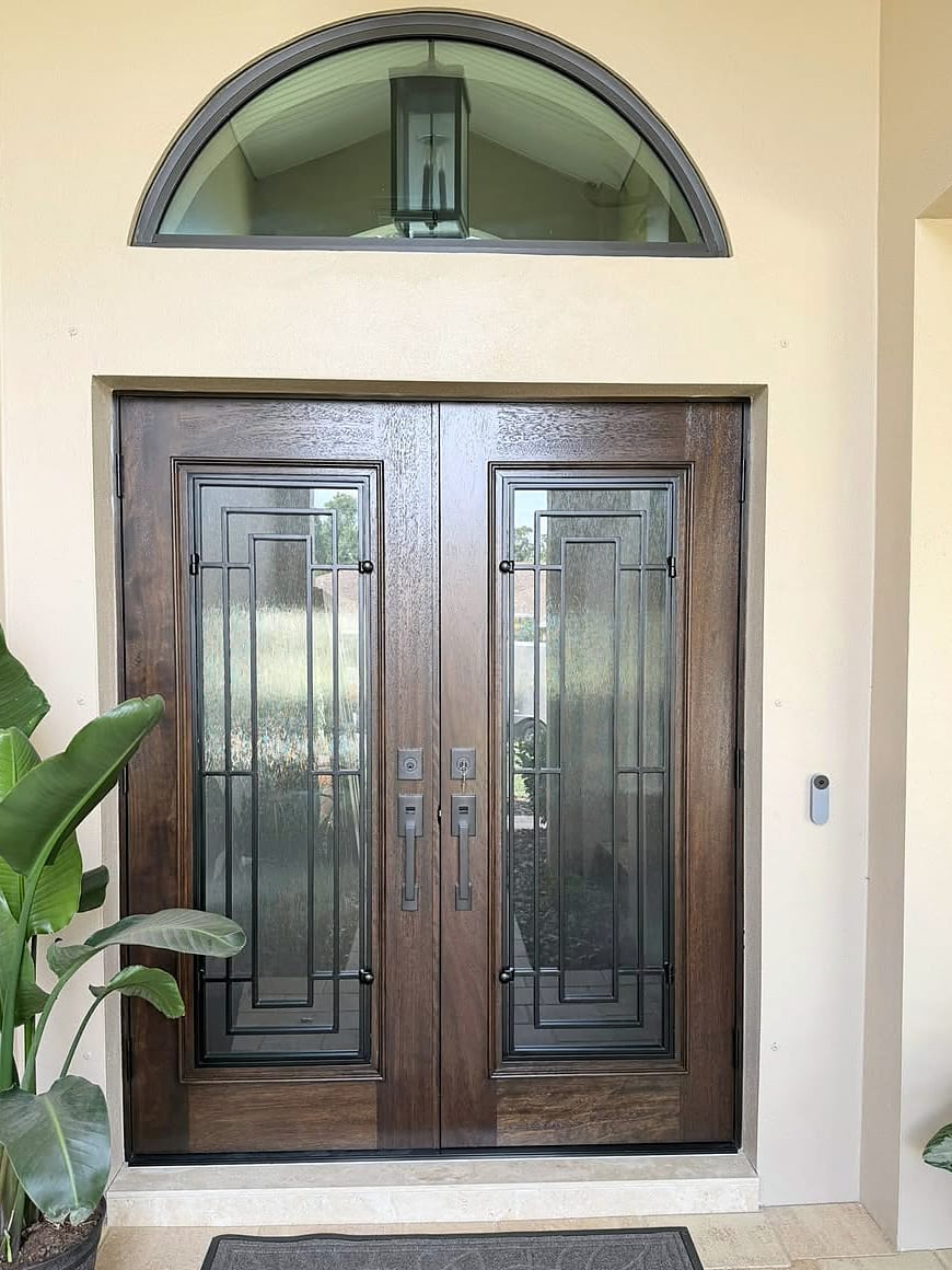 A stained hardwood double entry door with geometric leaded glass under a half-round transom