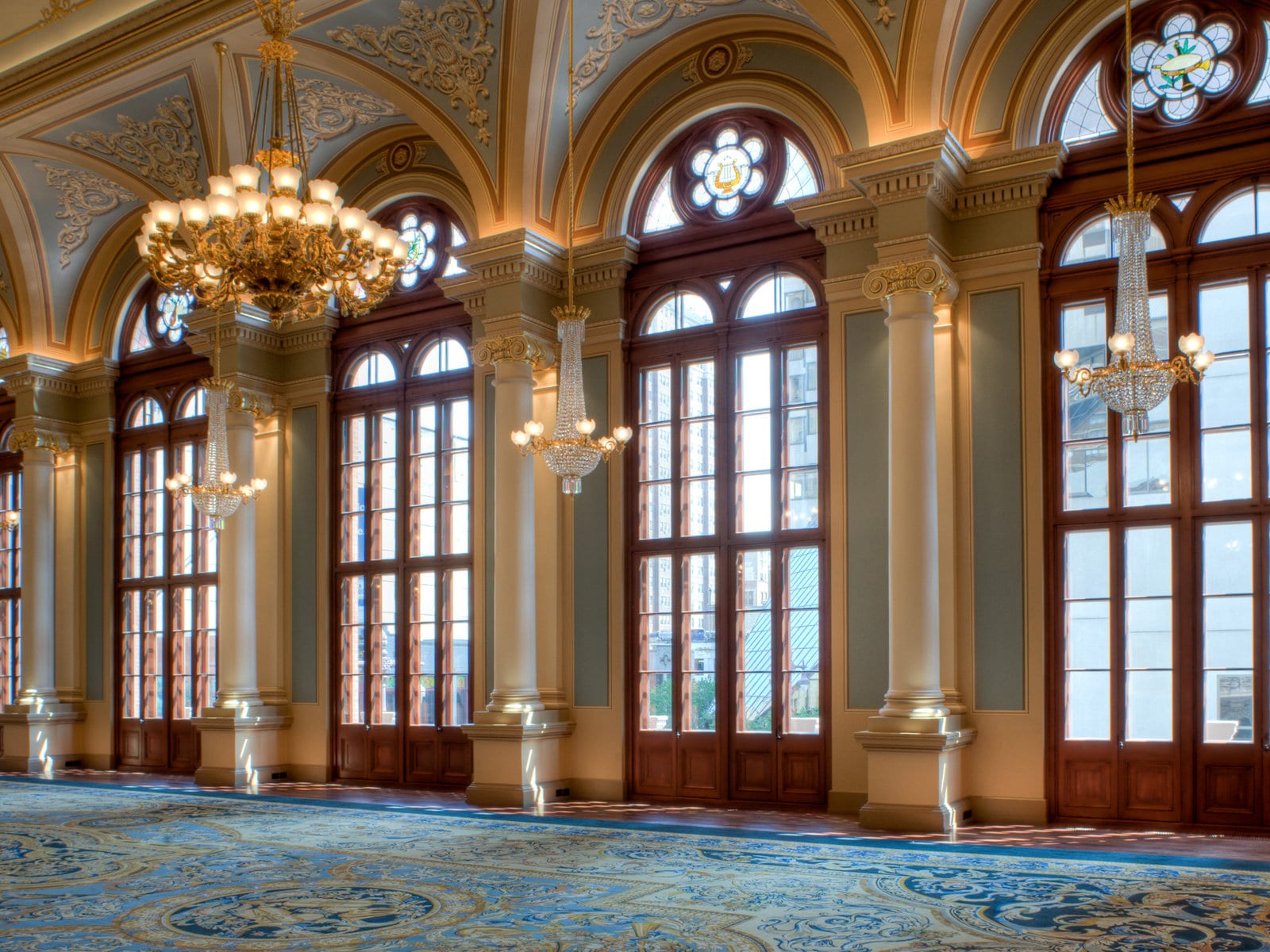 A grand ballroom with tall arched mahogany French doors and stained-glass transoms